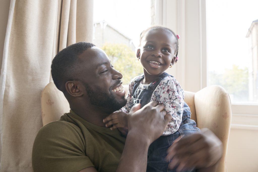 Young African man and daughter sitting in armchair and cuddling